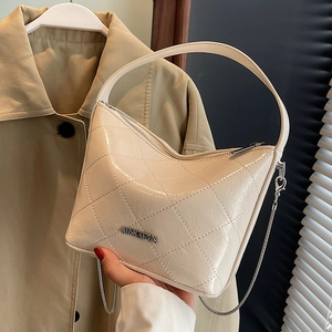 Quilted cream chain bag with glossy finish and silver strap held against a trench coat