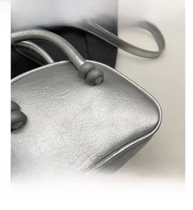 Detail of silver metallic leather handbag with pleated texture and matte gray ball clasp