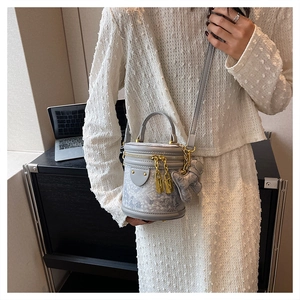 Detail of grey bucket bag featuring mountain embroidery, gold hardware, and bear charm