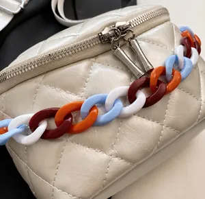 Detail of quilted white bag featuring a colorful acrylic chain and silver dual zippers