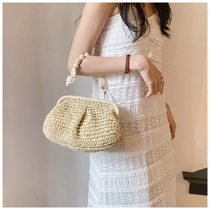 Detail of cream woven straw bag featuring a pearl and marble bead handle on white lace dress