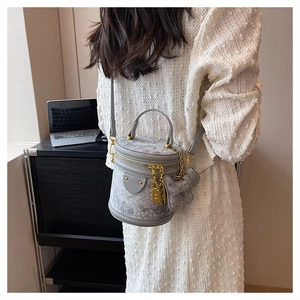 Detailed view of gray toile de jouy bucket bag with gold lock charms on white dress