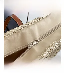 Detailed macro of smooth metal zipper and leather trim on woven straw tote bag