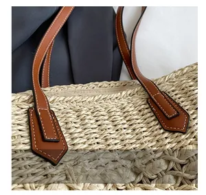 Close-up of high-quality stitching on the brown leather handle of a woven straw beach bag