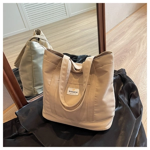 Close-up of beige canvas tote bag showing the logo tag and durable wide shoulder straps