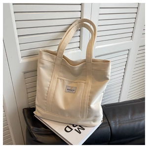 Detail of off-white canvas tote bag featuring front pocket and brand label on white background