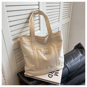Detailed shot of off-white canvas tote bag featuring textured fabric and grey logo label