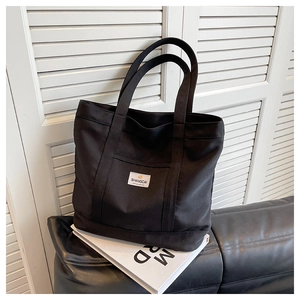 Detail of black canvas tote bag with woven label on a leather sofa and white books