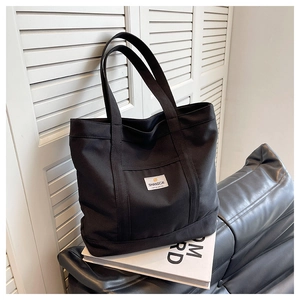 Close-up of black canvas tote bag featuring a white logo patch and sturdy double handles