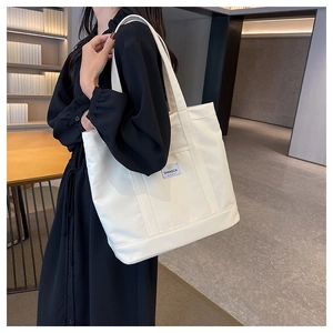 Detail showing the large canvas tote bag with wide strap and side pocket on a model