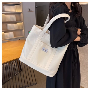 Minimalist cream canvas tote bag with shoulder straps worn by model in a library setting