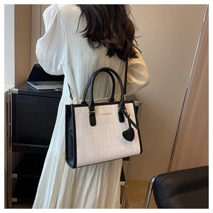 Détail d'un sac cabas matelassé noir et blanc avec breloque cœur porté par un mannequin