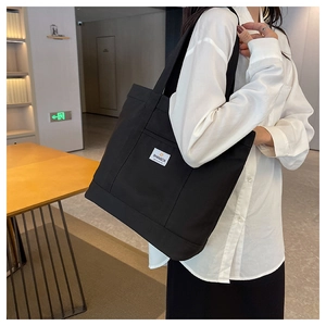 Detailed view of black canvas tote bag worn by model showing large capacity and front pocket