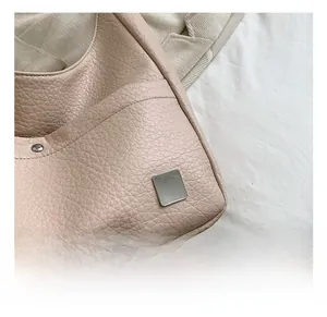 Detail showing litchi grain texture and square silver metal hardware on a beige bag