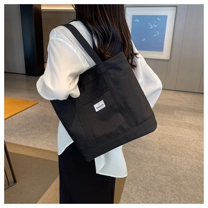 Detailed close-up of a large black canvas tote bag with side pocket and logo on the shoulder