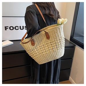 Close-up of handwoven straw tote bag with brown leather handles and textured weave detail