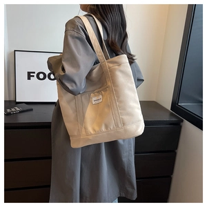 Detail of a large beige canvas tote bag with a small rectangular logo label on a shoulder strap