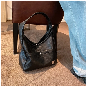 Detail of black pleated leather shoulder bag with silver metal logo in casual setting