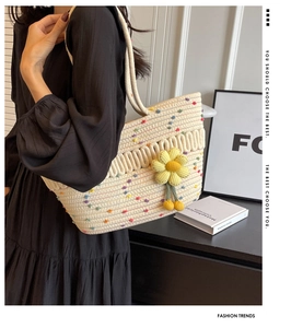 Detail of woven cream tote bag with colorful pom-poms and yellow sunflower charm