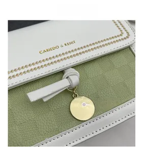 Dettaglio di cuciture in pelle bianca e verde menta con logo dorato e ciondolo