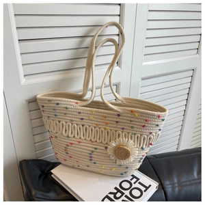 Detail of cream woven tote bag with colorful pom poms and daisy charm on a chair