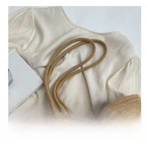 Detail of the thick woven rope shoulder strap on a light brown straw crossbody bag