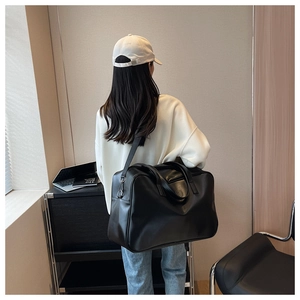 Rear view of model carrying a large black travel bag with adjustable strap and top handles