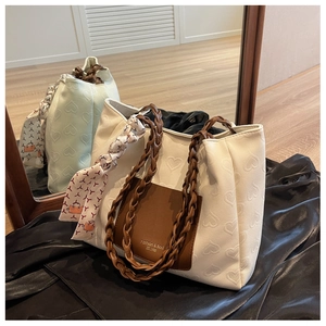 Detail of white heart-embossed tote bag with brown pocket and woven leather handle