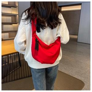 Détail d'un grand sac bandoulière en nylon rouge en forme de croissant porté par un mannequin