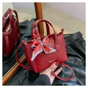 Close-up of red leather bucket bag with decorative scarf handle and metal accents