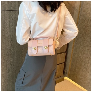 Détail du petit sac carré rose clair texturé avec fermoirs dorés et texte de mode élégant