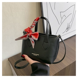 Close-up of black leather bucket bag featuring a red plaid bow and golden lettering