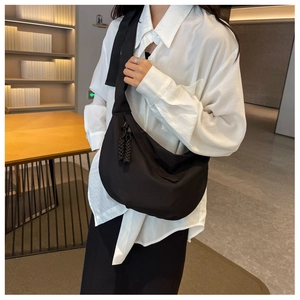 Détail d'un sac bandoulière croissant en nylon noir avec pompon tressé et fermeture