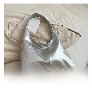 Détail d'un sac Boston argenté avec texture plissée posé sur un tissu tricoté