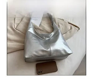 Comparaison de taille du sac hobo argenté avec un téléphone montrant sa grande capacité