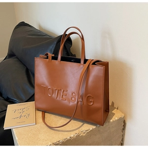 Détail du sac cabas en cuir marron avec lettrage gaufré sur un piédestal en pierre