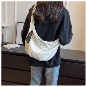 Détail du sac bandoulière en nylon crème avec étiquette latérale rouge distinctive