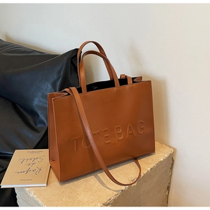 Gros plan du sac fourre-tout marron avec lettrage embossé sur un socle en pierre