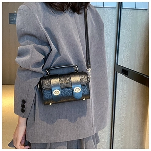 Détail d'un sac bandoulière noir effet crocodile et fermoirs dorés porté sur un blazer