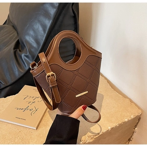 Gros plan d'un sac seau en cuir grainé marron avec barre dorée et poignée circulaire