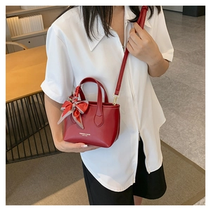 Detail of red PU leather bucket bag with a striped silk scarf tied on the handle