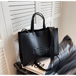 Détail du sac cabas en cuir noir avec texte TOTE BAG embossé et doubles anses