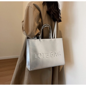 Gros plan d'un cabas argenté avec texte TOTE BAG embossé porté par un mannequin
