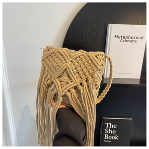 Detail of hand-woven beige straw bag with cotton tassels and bohemian diamond pattern