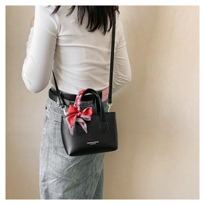 Detail of black crossbody bag with silk scarf on handle worn by a model