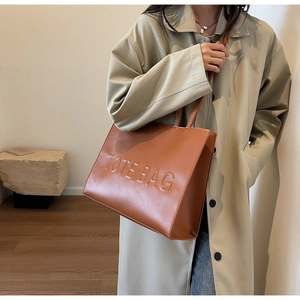 Sac fourre-tout en cuir marron avec texte embossé porté avec un trench-coat beige