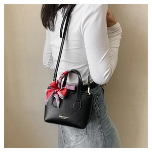 Detail of black crossbody bag featuring gold lettering and checkered ribbon on the handle