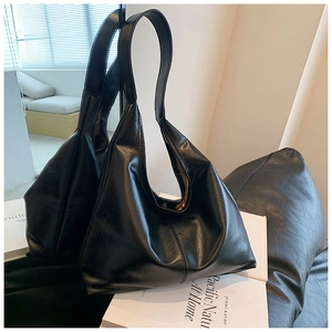 Détail d'un sac hobo en cuir huilé noir brillant posé sur une pile de livres blancs