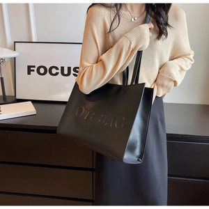 Détail d'un grand cabas en cuir noir avec texte embossé et une longue bandoulière réglable