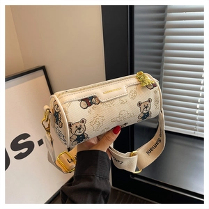 Vue détaillée d'un sac cylindrique crème avec pendentif ours et bandoulière large
